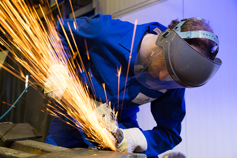 A man wearing protective gear while using an angle grinder producing a lot of sparks.